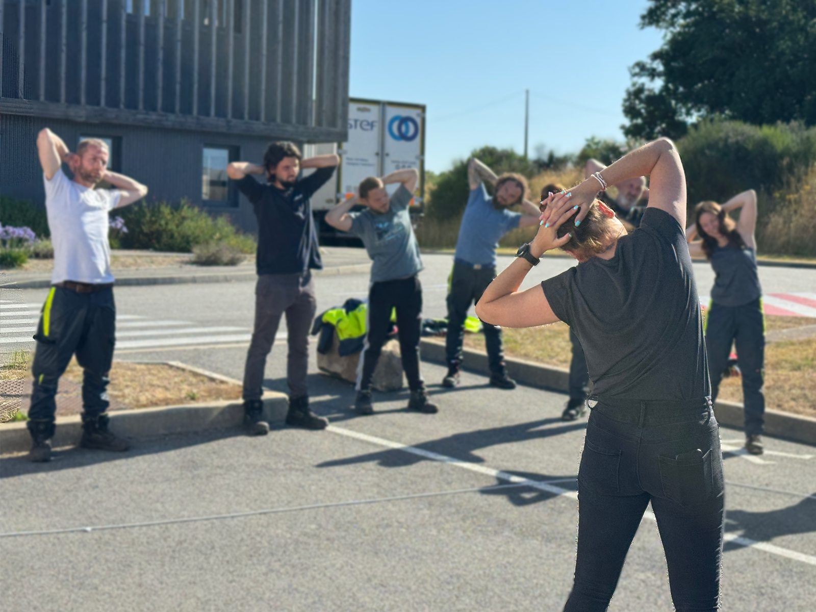 Groupe de salariés effectuant une pause active en extérieur sur site logistique avec un coach CF Prévention